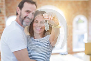 Middle age senior romantic couple holding and showing house keys smiling happy for moving to a new home