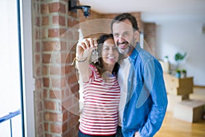 Middle age senior romantic couple holding and showing house keys smiling happy for moving to a new home