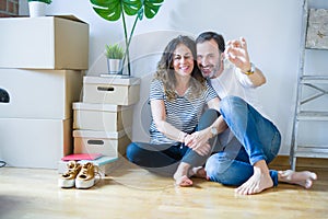 Middle age senior romantic couple in love sitting on the apartment floor with cardboard boxes around and showing house keys