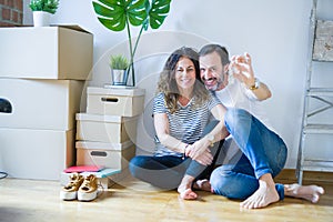 Middle age senior romantic couple in love sitting on the apartment floor with cardboard boxes around and showing house keys