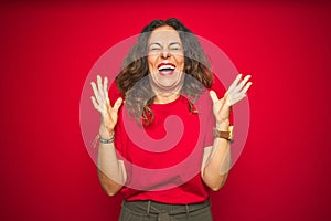 Middle age senior woman with curly hair over red isolated background celebrating mad and crazy for success with arms raised and