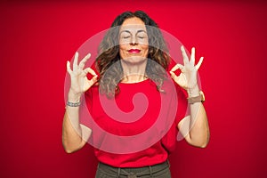 Middle age senior woman with curly hair over red isolated background relax and smiling with eyes closed doing meditation gesture