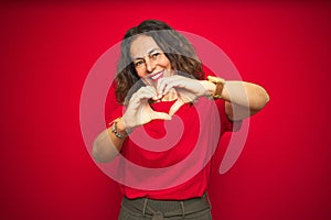 Middle age senior woman with curly hair over red isolated background smiling in love showing heart symbol and shape with hands