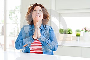 Middle age senior woman with curly hair wearing denim jacket at home begging and praying with hands together with hope expression