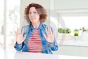 Middle age senior woman with curly hair wearing denim jacket at home Moving away hands palms showing refusal and denial with