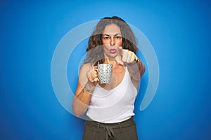 Middle age senior woman drinking a cup of coffee over blue isolated background pointing with finger to the camera and to you, hand