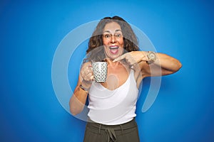 Middle age senior woman drinking a cup of coffee over blue isolated background very happy pointing with hand and finger