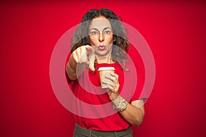 Middle age senior woman drinking a cup of coffee over red isolated background pointing with finger to the camera and to you, hand
