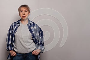 Middle age senior woman in grey t-shirt standing against grey studio wall background