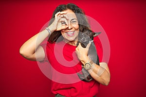 Middle age senior woman holding cute chihuahua dog over red isolated background with happy face smiling doing ok sign with hand on