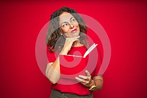 Middle age senior woman reading a book over red isolated background serious face thinking about question, very confused idea