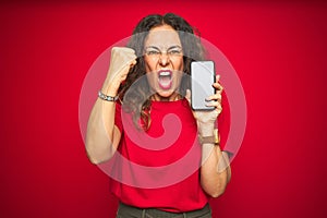 Middle age senior woman showing screen of smartphone over red isolated background annoyed and frustrated shouting with anger,