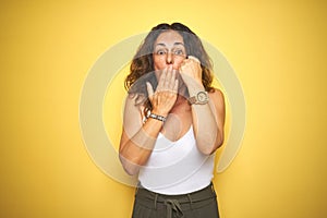 Middle age senior woman showing wrist watch over yellow isolated background cover mouth with hand shocked with shame for mistake,