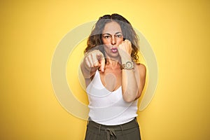 Middle age senior woman showing wrist watch over yellow isolated background pointing with finger to the camera and to you, hand