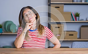 Middle age senior woman sitting at the table at home with hand on chin thinking about question, pensive expression