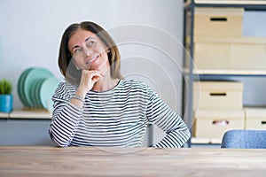 Middle age senior woman sitting at the table at home with hand on chin thinking about question, pensive expression