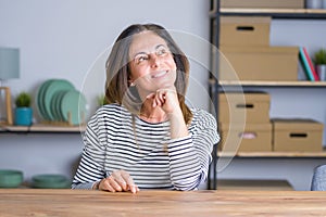 Middle age senior woman sitting at the table at home with hand on chin thinking about question, pensive expression