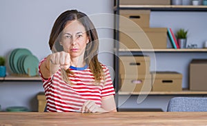 Middle age senior woman sitting at the table at home Punching fist to fight, aggressive and angry attack, threat and violence