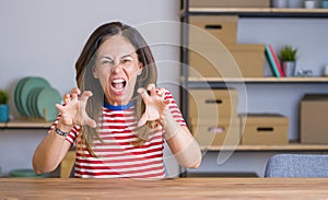 Middle age senior woman sitting at the table at home smiling funny doing claw gesture as cat, aggressive and sexy expression