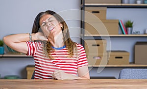 Middle age senior woman sitting at the table at home Suffering of neck ache injury, touching neck with hand, muscular pain