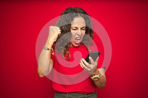 Middle age senior woman using smartphone over red isolated background annoyed and frustrated shouting with anger, crazy and