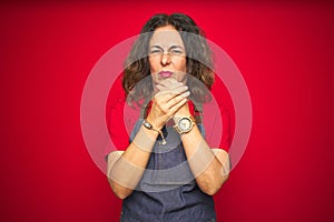 Middle age senior woman wearing apron uniform over red isolated background Suffering pain on hands and fingers, arthritis