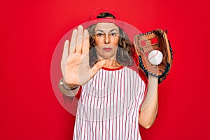 Middle age senior woman wearing baseball equiment, ball and glove over red isolated background with open hand doing stop sign with