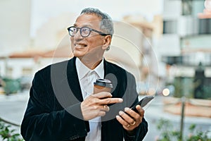 Middle age southeast asian man smiling using smartphone and drinking a cup of coffee at the city