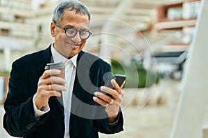 Middle age southeast asian man smiling using smartphone and drinking a cup of coffee at the city