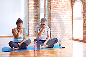 Middle age sporty couple sitting on mat doing stretching yoga exercise at gym tired rubbing nose and eyes feeling fatigue and