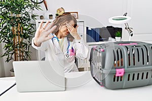 Middle age veterinarian woman working at pet clinic covering eyes with hands and doing stop gesture with sad and fear expression