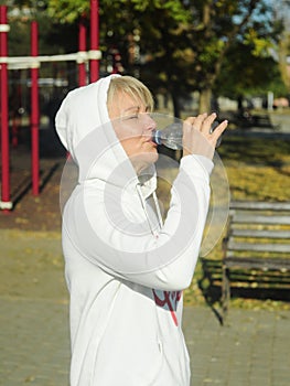 Middle age woman, 50 years, with a headphones drinking water on the playground