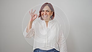 Middle age woman doing ok gesture smiling over isolated white background