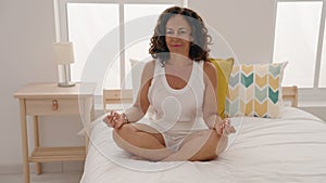 Middle age woman doing yoga exercise sitting on bed at bedroom