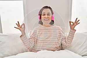 Middle age woman doing yoga exercise sitting on bed at bedroom