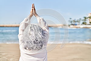 Middle age woman doing yoga exercise standing at seaside