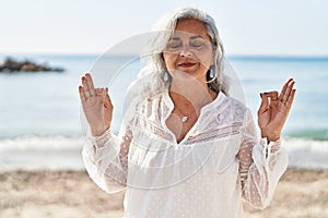 Middle age woman doing yoga exercise standing at seaside