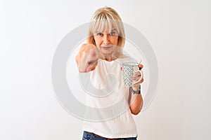 Middle age woman drinking cup of coffee standing over isolated white background pointing with finger to the camera and to you,