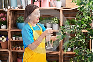 Middle age woman florist using diffuser working at flower shop