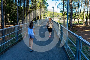 Middle-age woman and girl walking on an asphalt path with metal fences on the sides that runs through a pine forest
