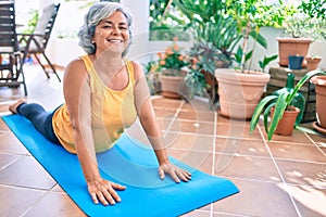 Middle age woman with grey hair smiling happy doing exercise and stretching on the terrace at home