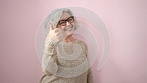 Middle age woman with grey hair smiling with thumbs up over isolated pink background