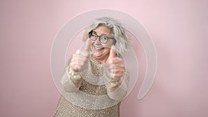 Middle age woman with grey hair smiling with thumbs up over isolated pink background