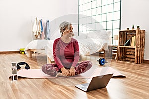 Middle age woman with grey hair training at home looking at exercise video on laptop looking to side, relax profile pose with