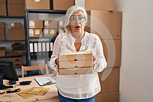 Middle age woman with grey hair working at small business ecommerce clueless and confused expression