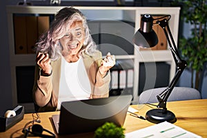 Middle age woman with grey hair working using computer laptop late at night celebrating surprised and amazed for success with arms