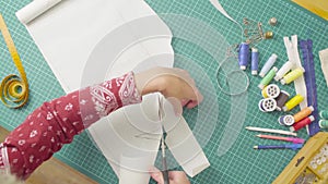 Middle-age woman hands with scissors cutting paper template. Handmade cloth.