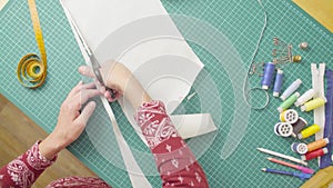 Middle-age woman hands with scissors cutting paper template. Handmade cloth.