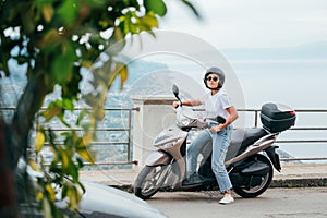 Middle-age woman in helmet and sunglasses on motor scooter on the Sicilian old town streets in the Forza d`Agro with Sant`Alessi