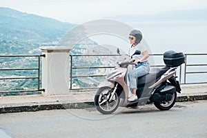 Middle-age woman in helmet and sunglasses on motor scooter on the Sicilian old town streets in the Forza d`Agro with Sant`Alessi photo